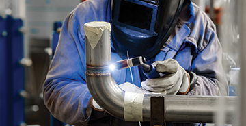 Industrial welder joining metal pipes in a fabrication shop